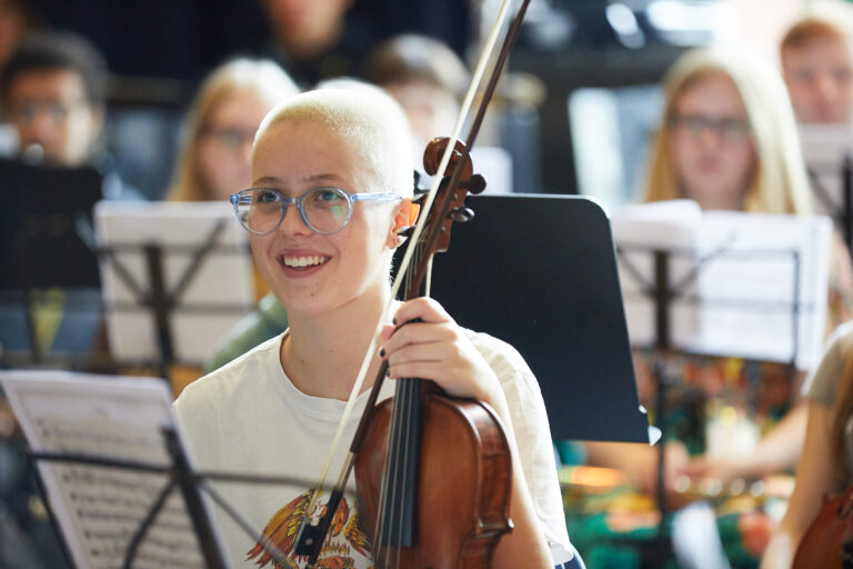 Teenage violinist at NYO Unite smiles while holding violin.